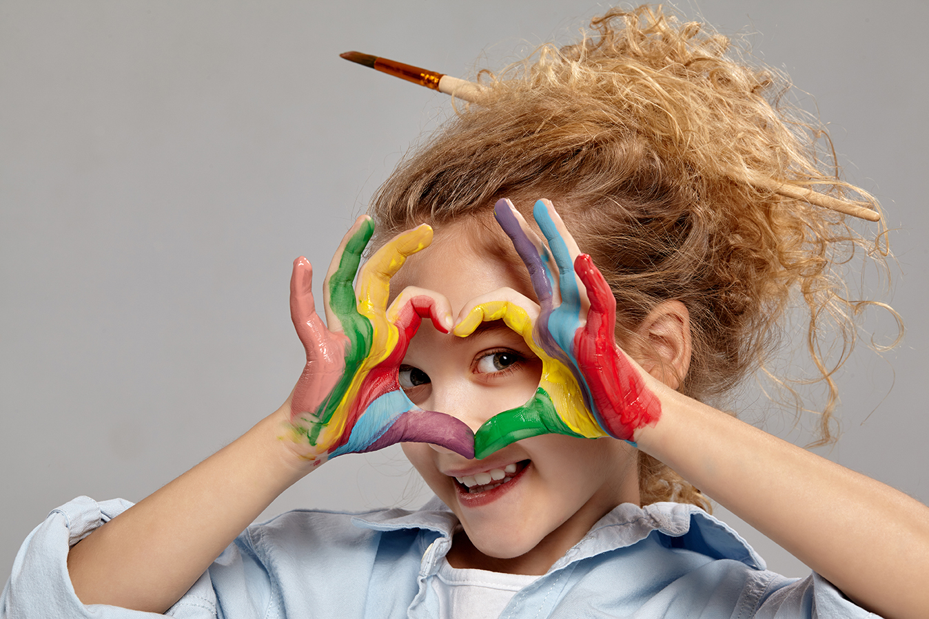 Little girl making a heart with her rainbow painted hands